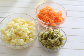 Нарезанные кусочками картофель натертые соленые огурцы и морковь для супа